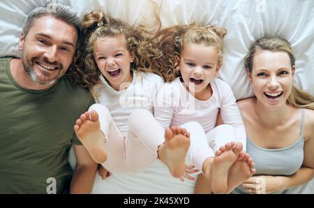 Vue de dessus, heureux et famille avec des jumeaux dans le lit souriant avec les parents le matin à la maison le week-end. Les enfants, le sourire et les filles espiègles aiment Banque D'Images