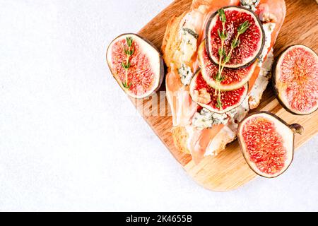 Bruschetta croissant frais avec figue mûre, fromage bleu, prosciutto, noix et herbes sur fond de table en béton blanc avec espace de copie. Santé bre Banque D'Images