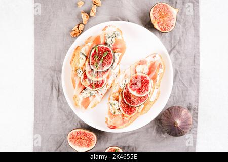 Bruschetta croissant frais avec figue mûre, fromage bleu, prosciutto, noix et herbes sur fond gris avec espace de copie. Idée de petit déjeuner sain. Sél Banque D'Images