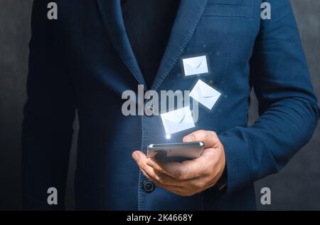 Homme d'affaires tenant un téléphone mobile et vérifiant des e-mails en ligne avec la technologie d'interface virtuelle. Homme mains utilisant le téléphone portable avec des enveloppes volantes. Direct Banque D'Images