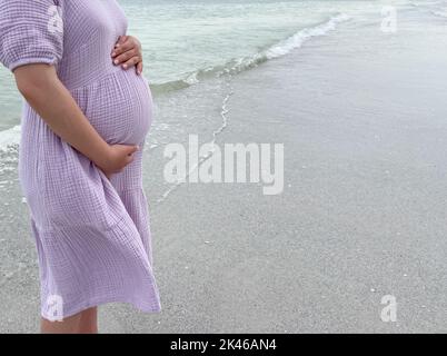 Plan d'une femme enceinte debout sur la plage avec sa main tenant son ventre - grossesse, attente, concept de maternité Banque D'Images