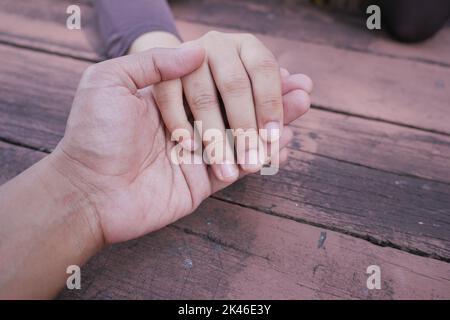 Gros plan d'un couple tenant les mains contre un fond orange. Banque D'Images