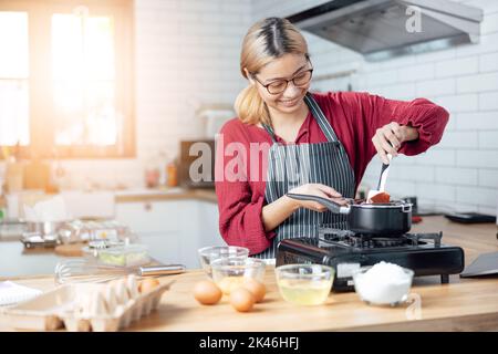 Belle jeune femme mélange batter, regardant l'appareil photo et sourire tout en cuisinant dans la cuisine à la maison, décorant un gâteau de gâteau au chocolat, la cuisine cl Banque D'Images