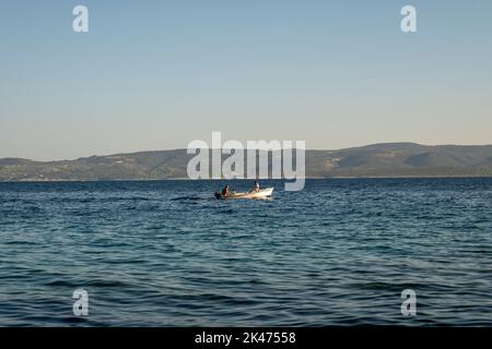 Les gens dans le bateau à moteur passent lentement au-dessus de la mer Adriatique calme, au large de la côte de Mimice, avec l'île de Brac visible au loin Banque D'Images