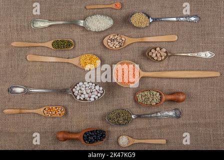 Source de protéines végétaliennes. Différentes sortes de légumineuses, lentilles, pois chiches et haricots dans différentes cuillères sur table en bois. Vue du dessus. Banque D'Images