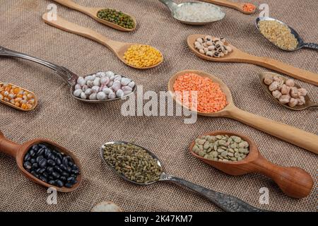 Source de protéines végétaliennes. Différentes sortes de légumineuses, lentilles, pois chiches et haricots dans différentes cuillères sur table en bois. Vue du dessus. Banque D'Images