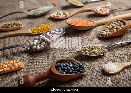 Source de protéines végétaliennes. Différentes sortes de légumineuses, lentilles, pois chiches et haricots dans différentes cuillères sur table en bois. Vue du dessus. Banque D'Images