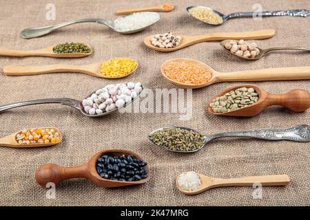 Source de protéines végétaliennes. Différentes sortes de légumineuses, lentilles, pois chiches et haricots dans différentes cuillères sur table en bois. Vue du dessus. Banque D'Images