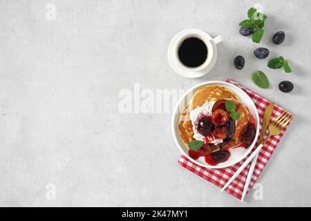 Crêpes avec prunes caramélisées avec feuilles de menthe et une tasse de café sur bakground gris. Vue sur le dessus, espace copie. Concept petit déjeuner du matin Banque D'Images
