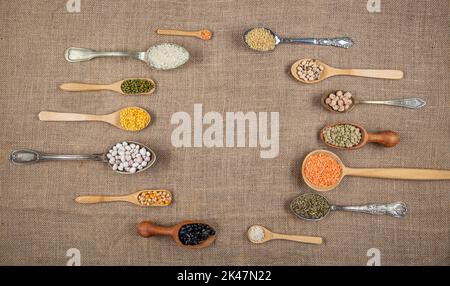 Source de protéines végétaliennes. Différentes sortes de légumineuses, lentilles, pois chiches et haricots dans différentes cuillères sur table en bois. Vue du dessus. Banque D'Images