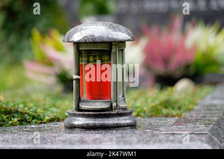 lanterne grave avec bougie rouge sur une tombe devant une décoration de fleur dans un fond flou Banque D'Images