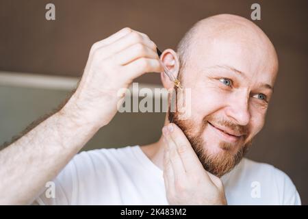 Homme beau adulte avec pipette avec huile de barbe dans la salle de bains à la maison Banque D'Images