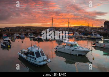 Les nuages s'allument en orange au lever du soleil, au-dessus du port, dans la station balnéaire de West Bay à Dorset. Banque D'Images