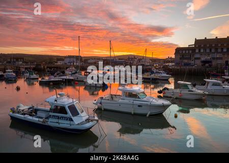 Les nuages s'allument en orange au lever du soleil, au-dessus du port, dans la station balnéaire de West Bay à Dorset. Banque D'Images