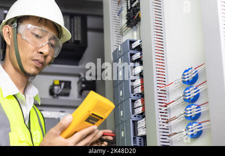 Un électricien mâle travaille dans un tableau de commutation, boîte à bornes électrique. Panneau de commande avec contacteur magnétique et relais de surcharge, mesure de la tension en ma Banque D'Images