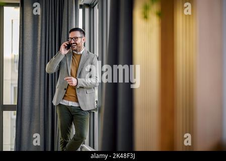 Ravi employé de bureau adulte, ayant une conversation avec son collègue au téléphone, riant. Banque D'Images