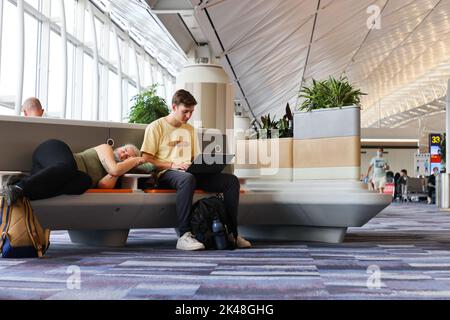 Homme et femme caucasiens dorment ou utilisent un ordinateur en attendant que l'avion embarque à l'aéroport international de Hong Kong Banque D'Images