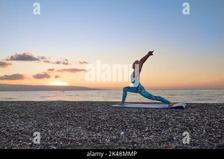 Jeune femme pratiquant le yoga sur la plage au lever du soleil, faisant Virabhadrasana ou posture du guerrier.harmonie, bien-être, méditation, style de vie sain, détente Banque D'Images