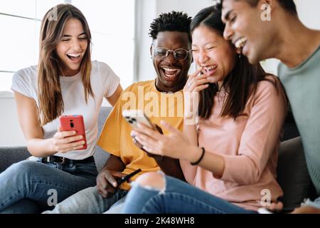 Jeune groupe d'amis divers assis sur un canapé à l'aide d'un téléphone portable Banque D'Images