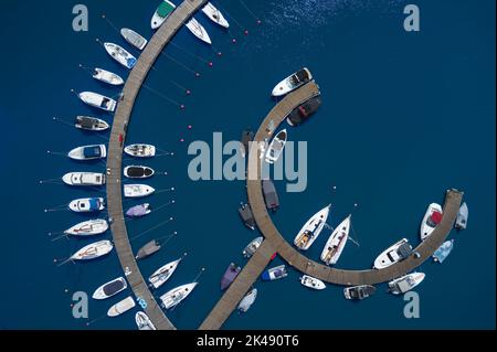 Vue aérienne des bateaux amarrés le long d'une jetée courbe sur l'eau bleue. Banque D'Images