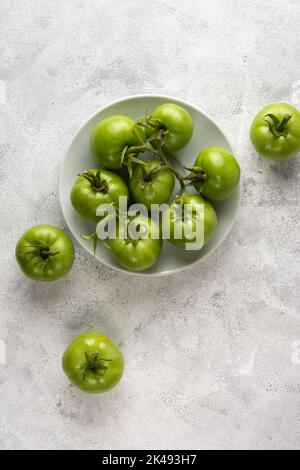 tomates sur une assiette blanche, baies vertes fraîchement récoltées éparpillées sur une surface de table texturée, prises par le dessus avec un espace de copie Banque D'Images