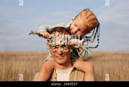 Papa et fille. L'homme joue avec une petite fille dans la nature. Enfant aux cheveux rouges près des yeux des pères avec des fleurs Banque D'Images