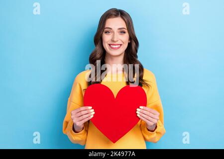 Photo de jeune attrayant magnifique jolie belle femme porter jaune chandail Toothy sourire tenir papier cœur rouge sentiments date isolé sur la couleur bleue Banque D'Images