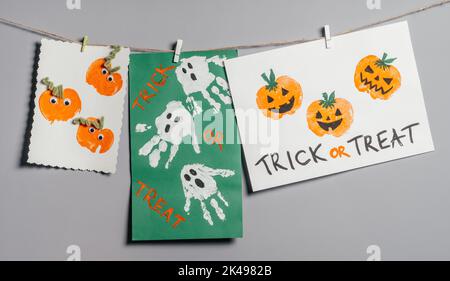 Trois reproductions de pommes de citrouille et de fantômes d'Halloween pour enfants dessins accrochés à la corde sur un mur gris avec inscription Trick or Treat. Fait à la main Banque D'Images