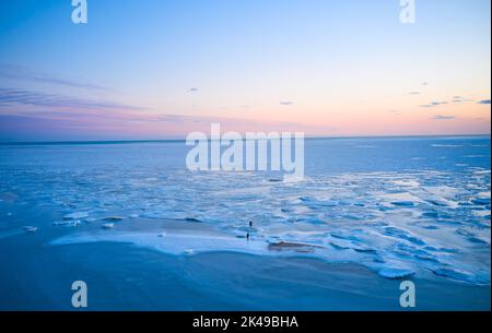 Vue aérienne - deux personnes marchent sur la glace au coucher du soleil sur la mer gelée. Paysage hivernal sur la mer au crépuscule. Vue depuis le dessus de la fonte de glace dans l'océan Banque D'Images