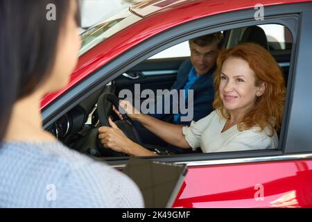 Couple charmant testant l'intérieur de la voiture et discutant avec le conseiller Banque D'Images