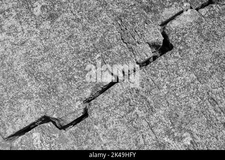 Grande fissure sur le mur gris. Défaut diagonal large et profond. Photo en noir et blanc. Gros plan. Copier l'espace. Mise au point sélective. Banque D'Images