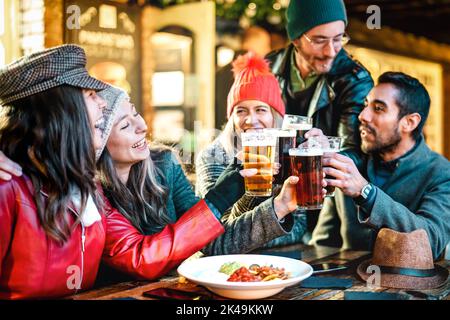 Des amis multiculturels heureux boivent de la bière avec des nachos à l'extérieur la nuit - concept de mode de vie de nourriture et de boissons sur les jeunes appréciant le temps ensemble o Banque D'Images