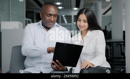 Divers partenaires d'affaires siègent au bureau discuter de l'instruction papier homme d'affaires africain montrer la documentation dans la tablette de dossier à la collègue arabe femelle Banque D'Images
