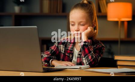 Lazy duty caucasien jeune enfant blond petite paresseuse fille fatigué étudiant la routine en ligne cours élémentaire d'éducation sur le nopping d'ordinateur portable à la maison Banque D'Images