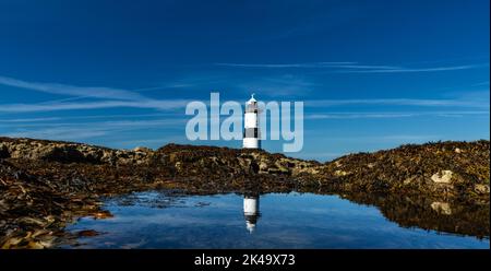 Une vue panoramique sur le phare de Penmon dans le nord du pays de Galles avec des relections dans une piscine à marée Banque D'Images
