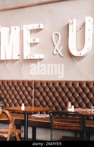 chaises et tables en bois à côté d'un canapé en cuir dans un café calme et propre avec de grandes lettres lumineuses sur le mur disant moi et u, le bar mylk, nouveau Banque D'Images