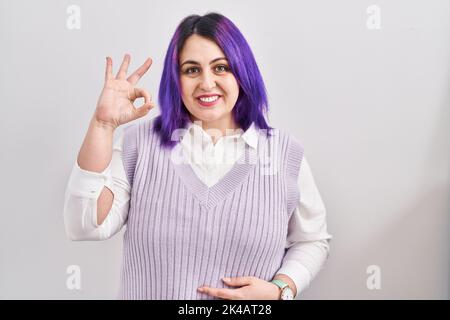 Plus taille femme avec cheveux violets debout sur fond blanc sourire positif faisant ok signe avec la main et les doigts. Expression réussie. Banque D'Images