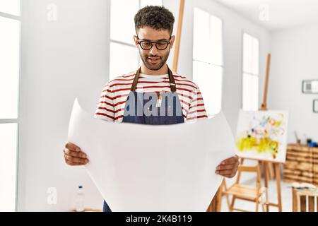 Jeune artiste arabe homme souriant heureux de tenir le dessin au studio d'art. Banque D'Images