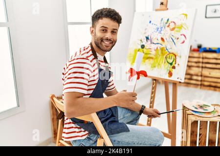Jeune artiste arabe homme souriant heureux titulaire d'un diplôme en studio d'art. Banque D'Images