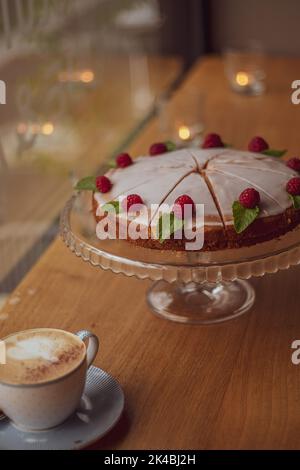 gâteau au glaçage blanc décoré de framboises fraîches et de feuilles de menthe sur une table en bois dans un café. Banque D'Images