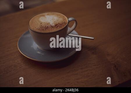 Tasse de café avec un motif de coeur dans une tasse sur une soucoupe sur un fond en bois dans un café. Banque D'Images