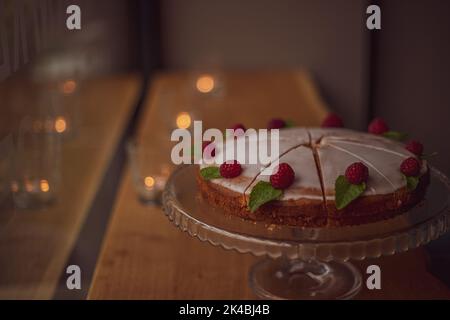 gâteau au glaçage blanc décoré de framboises fraîches et de feuilles de menthe sur une table en bois dans un café. Banque D'Images