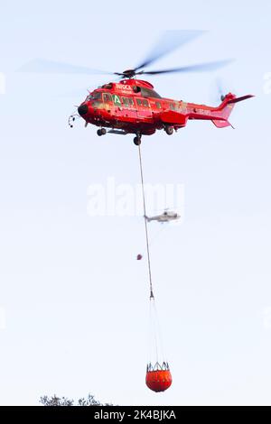 Un Airbus Red H215 remplit un seau d'eau alors qu'il combat le feu de forêt espagnol Estepona Banque D'Images