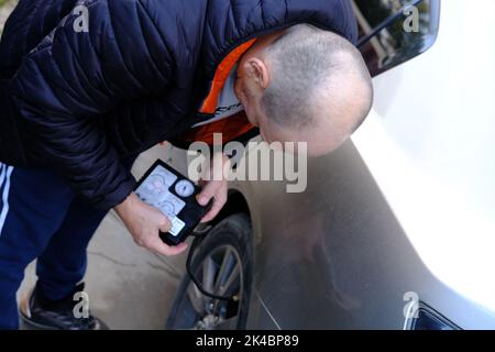 homme gonflant un pneu de voiture avec un compresseur d'air portatif dans la rue. Banque D'Images