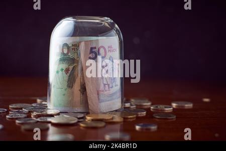 Une tasse de verre de fermeture sur des billets de Colombia Peso sur une table en bois avec des pièces de monnaie Banque D'Images