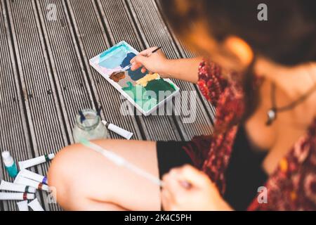 Jeune femme plongeant un pinceau dans une palette de peinture Banque D'Images