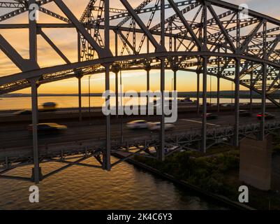 Un grand pont de treillis sur une vaste étendue d'eau est vu au coucher du soleil comme les voitures, mouvement flou, Voyage à travers l'autoroute à plusieurs voies. Banque D'Images