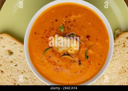 Image horizontale d'un bol de soupe aux tomates avec garniture, et pain blanc coupé en tranches sur l'assiette Banque D'Images