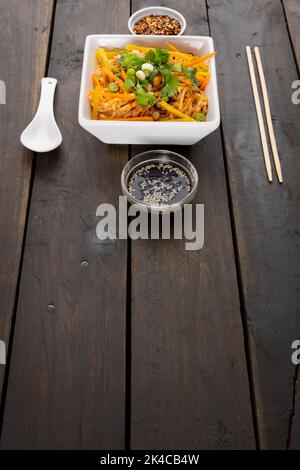 Gros plan sur du wok asiatique, faire sauter les nouilles avec des baguettes, une cuillère et des condiments sur le bois Banque D'Images