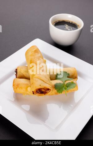 Gros plan des rouleaux de printemps asiatiques sur une assiette blanche et de la sauce soja sur fond gris Banque D'Images